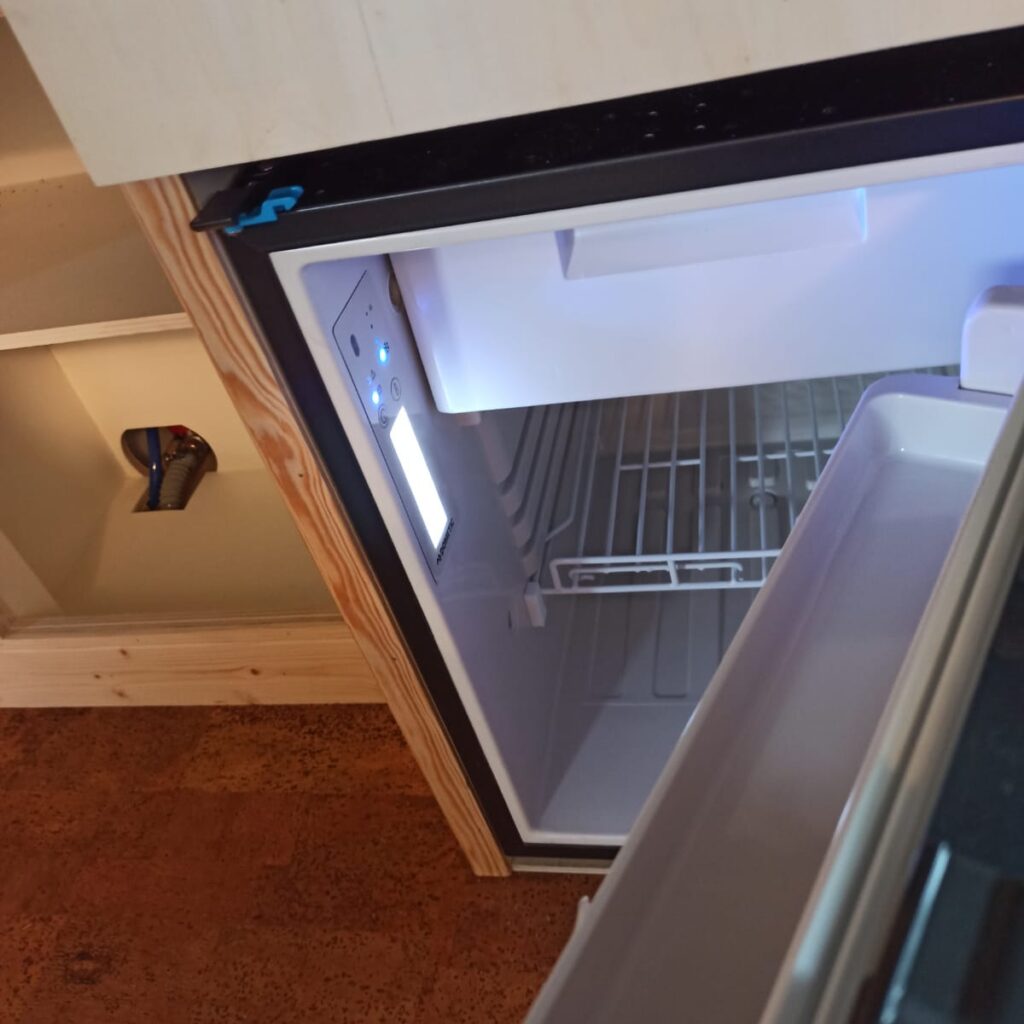 Close up van de ingebouwde compressiekoelkast met vriesvakje met het deurtje open, zodat je kunt zien dat deze het doet (de lichtjes branden aan de binnenkant)