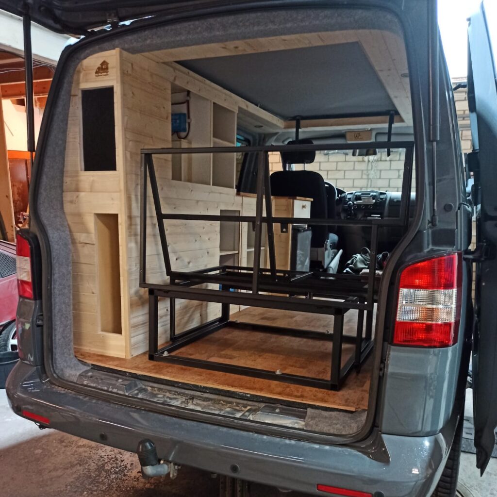 Het zwarte stalen frame van de bank (en daarmee het bed) is geplaatst, gezien vanaf de achterkant door de achterklep die open staat