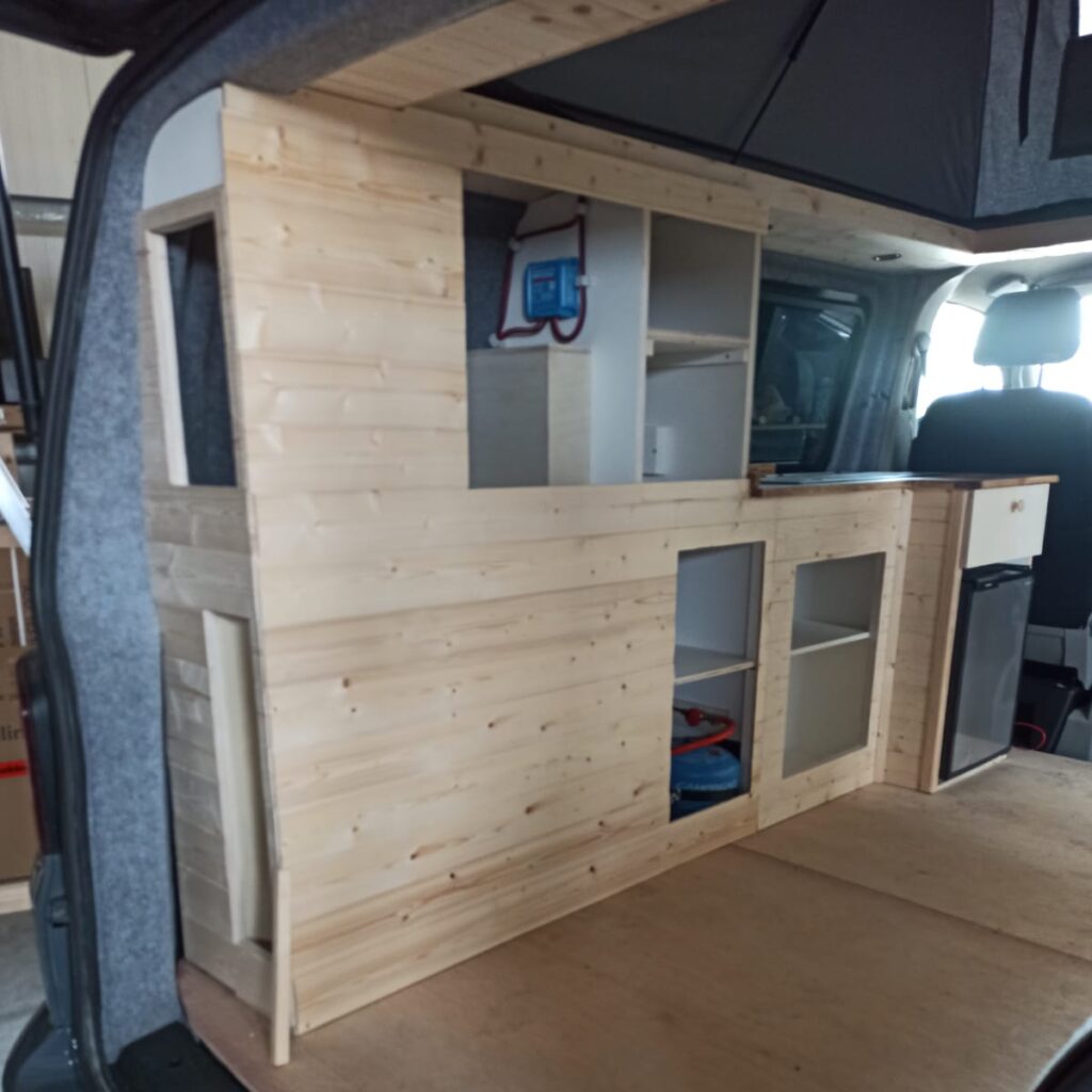 De wand met de kastjes en de keuken, nog zonder de deurtjes (wel al met koelkast), gezien vanaf de achterkant